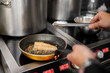 © pavel siamionov - A chef sears a sesame-crusted salmon fillet in a frying pan on a professional induction cooktop in a commercial kitchen