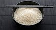 © Tufayel - A wooden spoon resting on a bowl filled with uncooked white rice grains.