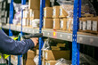 © Val - Warehouse operative using a handheld barcode scanner to scan a location label on a picking shelf, with stocked inventory visible on surrounding shelves