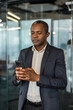 © Liubomir - Focused man in a business suit holding and typing on his mobile phone in a contemporary workspace, managing communications and staying connected for work tasks