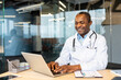 © Liubomir - African doctor smiling at computer while delivering telemedicine care and expert medical advice from a modern clinic, confident and professional in virtual patient consultation