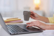 © New Africa - Woman with cup of drink using laptop at white table indoors, closeup