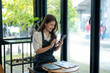 © apichat - Woman entrepreneur managing online business on smartphone at cafe