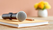 ©  VladaToday - Compact handheld microphone placed on notebook with pencil on wooden table for podcast interview background and voice recording setup image for media use