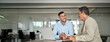 © insta_photos - Young smiling professional latin business man working in corporate office with older executive manager using laptop technology having conversation on financial project strategy at work meeting.