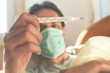 © Teodor Lazarev - Man checking thermometer for fever wearing face mask