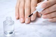 © MH24 - Close-up of a woman's hands meticulously applying clear nail polish to her fingernails, emphasizing natural beauty and nail care routine.