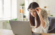 © Studio Romantic - Young woman leaning toward laptop and lifting glasses while struggling to read text. Focused female with myopia struggling with blurry vision, experiencing eye strain and discomfort while working.