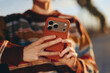 © SHOTPRIME STUDIO - Woman wearing a rainbow sweater holding a smartphone outdoors. The woman is smiling and using the device with both hands in natural sunlight. Casual lifestyle and technology concept.