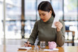 © David - A woman checks her expenses while managing finances, holding receipts and keeping track of savings with a piggy bank and coins on a wooden table.