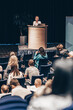© kasto - Female speaker giving a talk on corporate business conference. Unrecognizable people in audience at conference hall. Business and Entrepreneurship event