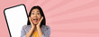 © Prostock-studio - A person shows excitement with wide eyes and a big smile. They hold their face with both hands. A blank mobile phone is visible next to them. The background is a plain pink color.