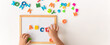© Prostock-studio - Hands of a child arrange colorful magnetic letters on a whiteboard. Some letters are scattered around on a flat surface. The activity focuses on teaching the alphabet and spelling skills.