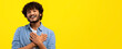 © Prostock-studio - A man stands in front of a bright yellow wall. He smiles widely and holds his hands over his heart. The setting looks casual and welcoming. The lighting is bright and cheerful.
