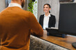 © Serhii - Smiling receptionist greeting guest at hotel desk