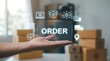 © MHS-AI - A hand forward, presenting a holographic display of the word 'ORDER' surrounded by various e-commerce, delivery, and logistics icons, set against a background of stacked cardboard shipping boxes.