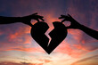 © Sarfraz - Hands holding broken heart against vibrant sunset sky
