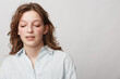 © SHOTPRIME STUDIO - Young woman with closed eyes and relaxed expression wears white shirt against plain background. Concept of calm, introspection, natural beauty, and peaceful moment in studio portrait.
