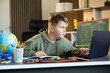 © Dejan - A young boy is intently studying his laptop and books at a modern, organized workspace.