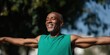 © Andrii Zastrozhnov - African male adult smiling with arms extended in green tank top under blue sky outdoors reflecting joy strength and healthy active lifestyle