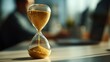 © Sutasinee - A glass hourglass standing on a desk, sand flowing. A businessman is working on a desk in a modern office background, symbol of time management, productivity, and deadline concept