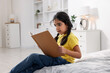 © New Africa - Cute little girl reading book on bed at home