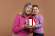 © New Africa - Little girl greeting her grandmother with gift on dark beige background