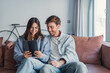 © Daniel - A happy young couple relaxes on a cozy couch while using a tablet together, smiling and hugging as they look at the screen, enjoying online shopping, browsing apps, or watching videos at home