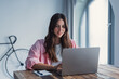 © Daniel - Happy young woman sit at desk look at laptop screen browsing surfing wireless Internet at home, smiling millennial female employee work on modern computer in living room, technology concept