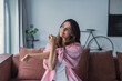 © Daniel - A young woman sitting on a cozy sofa at home gently stretches her arm using the other hand, relieving muscle stiffness and enjoying a calm self-care moment indoors