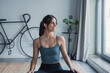 © Daniel - Brunette woman at home sitting on the floor on a carpet training yoga wearing sportswear. Young female dreamer looking outside smiling enjoying