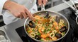 © Muhammad - Seafood Paella Preparation - Chef Stirring Shrimp, Mussels, and Calamari in Pan on Induction Cooktop.