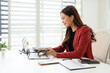 © Fahng - Asian business woman using laptop computer typing And working online sitting at desk in office wearing suit. Office worker lady browsing internet on computer. Entrepreneurship.