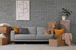 © Pixel-Shot - Stylish poster and sofa with cardboard boxes in room on moving day