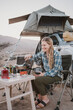 © Cavan Images - Smiling young woman makes dinner while overland camping in Oman
