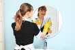 © Pixel-Shot - Smiling maid with detergent and rag cleaning mirror in bathroom