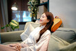 © Stella 16 - Woman uses neck massager pillow at home. She relaxes in chair with closed eyes enjoying gentle vibration therapy for neck pain relief and stress reduction. Cozy atmosphere