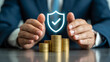 © Rajan - A businessman protects a stack of gold coins with a glowing shield symbol.