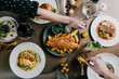 © Reuben - Overhead view of gourmet meal with fish, chips, and colorful side dishes. Hands reach for food, showing casual dining enjoyment. Plate arrangement suggests fine dining or celebratory gathering