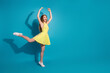 © deagreez - Stylish young woman in a vibrant yellow summer dress striking a playful pose against a vivid blue background