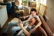 © Davor - Two men relaxing with smartphones on couch amid moving boxes at home