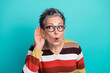© deagreez - Older woman with short gray hair and glasses listens closely against a blue studio background wearing a striped sweater and casual fashion style