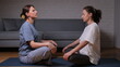 © Aliaksandr - Two women sitting on yoga mats, facing each other with eyes closed, finding peace and relaxation through a shared meditation practice in a comfortable home environment