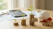 © Manu - Close-up of stacked coins increasing in height with small green seedlings growing on top, wooden house models and a white piggy bank placed nearby with a calculator in the background, soft neutral lig