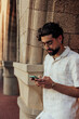 © bernardbodo - Fashionable man leaning on stone column in urban street, using smartphone and showing Gen Z lifestyle