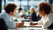 © Kateryna - Wide bright office scene of two professionals from behind seated at adjacent desks both leaning over shared notebooks in a focused collaborative discussion pens visible in both