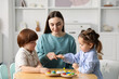 © New Africa - Mother and her children playing with toys at wooden table indoors