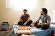 © AntonioDiaz - Young men enjoying pizza and beer in a casual room, roommates relaxing together in their basic apartment
