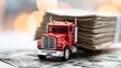 © The Little Hut - Red Toy Truck Carrying Stack of Money Represents Finance, Investment, Wealth, and Transportation Costs