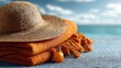 © DesignMint - A woven straw hat and vibrant orange beach towels with a small golden sunscreen bottle are arranged